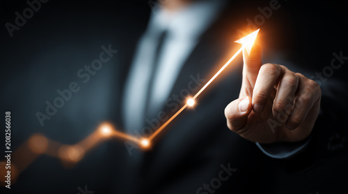 A businessman pointing at a glowing graph indicating upward growth and success in a dark background.