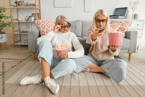 Mature female friends in 3D glasses with popcorn watching movie at home