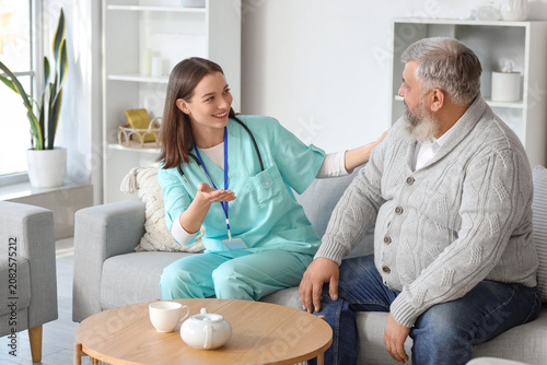 Mature man with nurse sitting on sofa at home