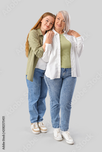 Young woman hugging her mother on light background