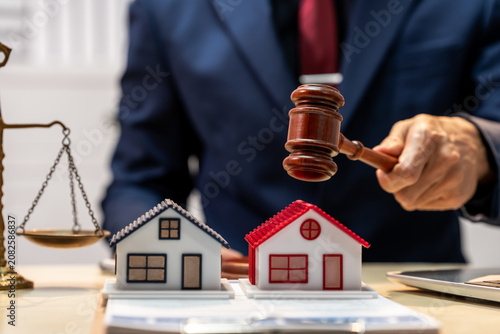 Lawyer holding gavel beside house models and scales of justice, showing property dispute or real estate law concept