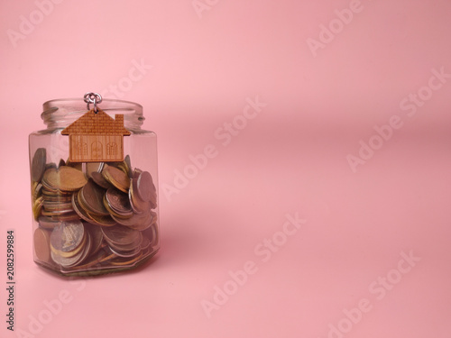 A glass jar packed tightly with metal coins features a wooden house-shaped charm attached to its rim
