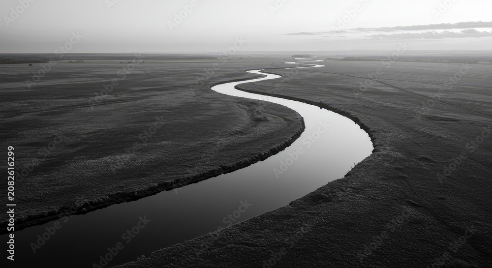 Fototapeta premium A serene river flows gently through a vast, dark landscape under a cloudy sky.