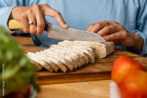 Hands Slicing Fresh Tempeh on a Wooden Cutting Board, Healthy Cooking Concept