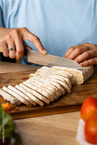 Hands Slicing Fresh Tempeh on a Wooden Cutting Board, Healthy Cooking Concept