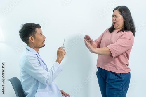Foto Female patient looks afraid and pulls back from a doctor holding a syringe during a medical visit, showing fear of injection, anxiety, and healthcare stress on a plain background