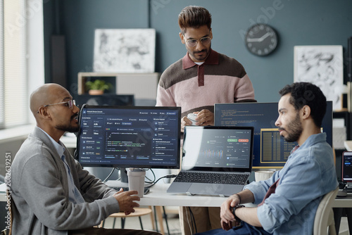 Canvas Print Multiethnic young adult men discussing software development workflow in information technology office, reviewing code and analytics dashboards