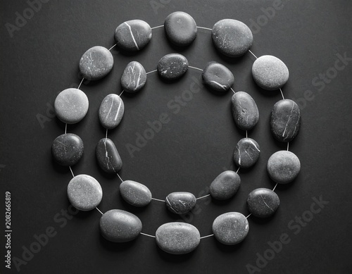 A necklace made of smooth, grey river stones arranged in a circular pattern on a dark background