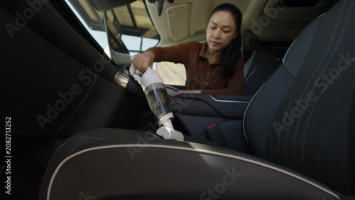 woman using a portable handheld vacuum cleaner to clean dust on leather car seat of electric car