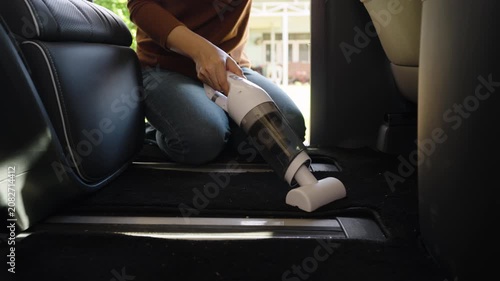 close up hand of woman using a portable handheld vacuum cleaner to cleaning the floor mat of her luxury car