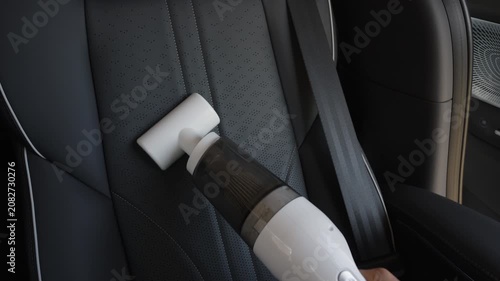 close up hand of woman using portable handheld vacuum cleaner to clean dust on leather car seat of electric car