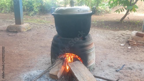 Traditional cooking using a wood burning stove in an outdoor area. A large pot is placed on the stove which is lit by a fire burning wood.