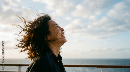 Asian woman laughing in wind by the sea