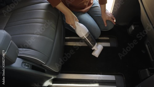 close up hand of woman using a portable handheld vacuum cleaner to cleaning the floor mat of her luxury car