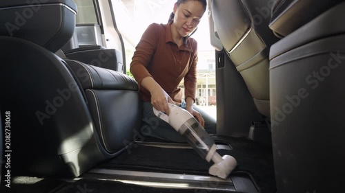 woman using portable handheld vacuum cleaner to cleaning the floor mat of her luxury car