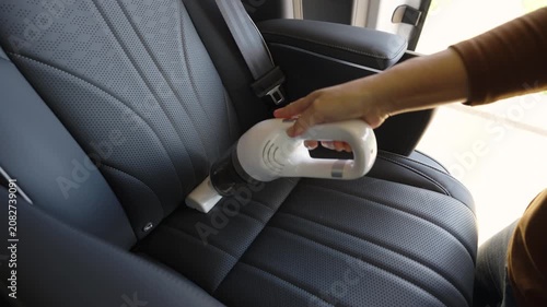 close up hand of woman using portable handheld vacuum cleaner to clean dust on leather car seat of electric car