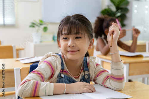 Canvastavla Smiling schoolgirl writes in notebook during classroom lesson, expressing confidence, curiosity and positive learning in elementary education environment with classmate nearby in school