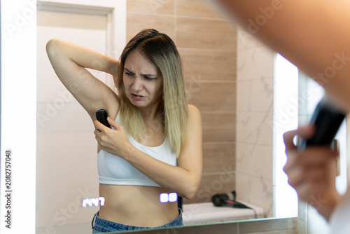 The bad smell of sweat from the armpits is a concept. displeased woman while applying deodorant on underarm