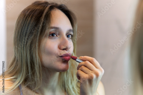 red lipstick in the hands of a woman. woman is meticulously applying lipstick in front of a mirror, focusing carefully on enhancing her appearance and striking a beautiful look