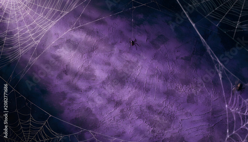 Spooky halloween background with spider webs and spiders on a textured dark purple wall