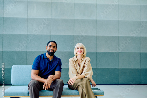 Fotografie Business colleagues of diverse ethnicity smiling and sitting on a bench in a con