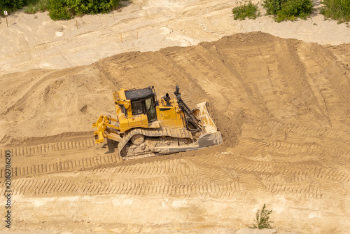 Heavy construction equipment moving limestone at Rummu Quarry, Estonia, surrounded by towering quarry walls and sandy terrain in an active mining site.