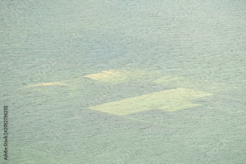 Aerial view of submerged buildings beneath crystal-clear turquoise water in Rummu Quarry, Estonia. Flooded limestone quarry creating an eerie underwater landscape with natural textures.