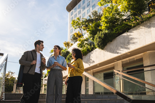 Photography Three business colleagues standing outdoors, having coffee, and discussing durin