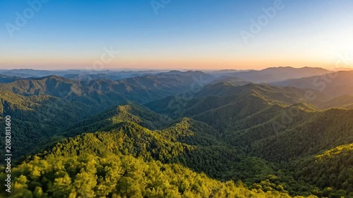 Aerial sunrise view over a mountain range with golden light on treetops.