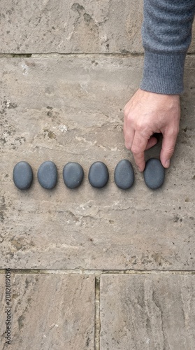 Hand placing smooth dark stones in a row