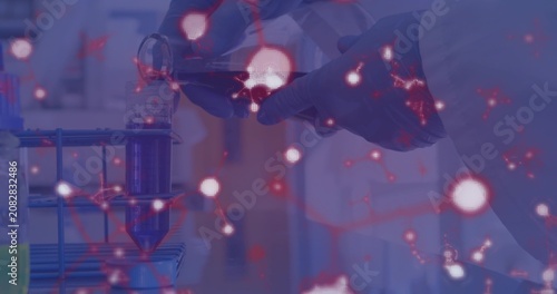 Gloved hands grasping vial and pouring purple fluid into tube for lab prep, particles drifting