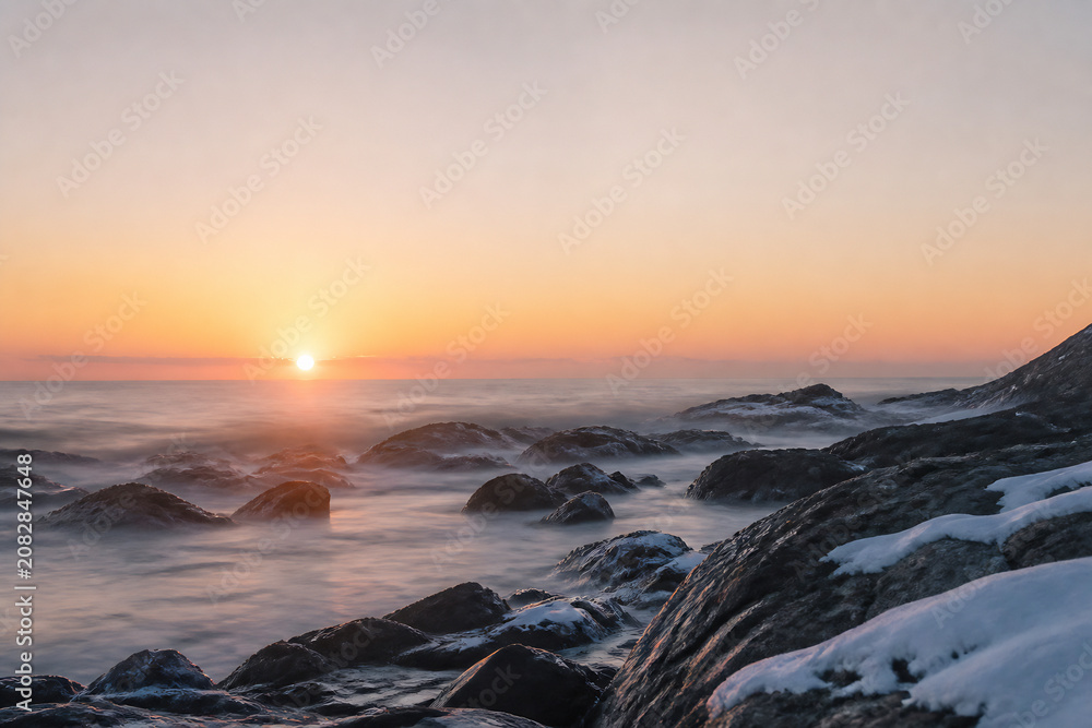Fototapeta premium A serene sunrise over a rocky coastline with gentle waves washing ashore.