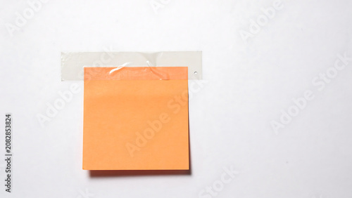 Blank orange sticky note taped on white wall with adhesive reminder stationery