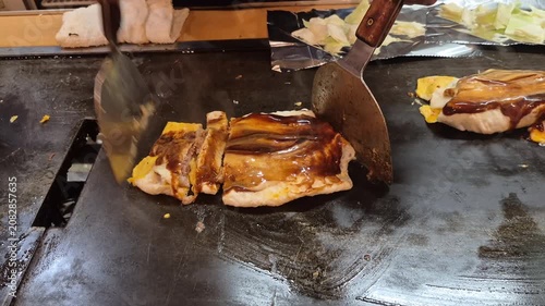 Cooking and cutting Okonoiyaki on teppan iron plate Osaka Japan traditional food