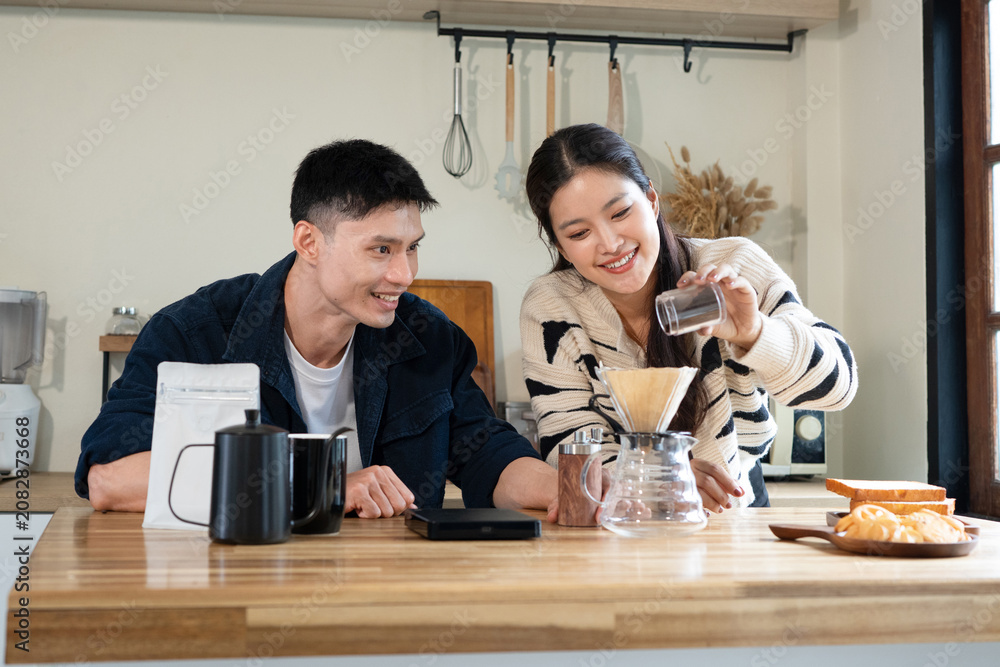 Fototapeta premium Happy Asian couple making a drip coffee brew in the kitchen together for breakfast, ideal for lifestyle and home living concepts.