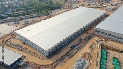 Canvastavla Construction of a large industrial warehouse under clear sky, showing modern architecture and industrial development, with surrounding infrastructure and ongoing building work