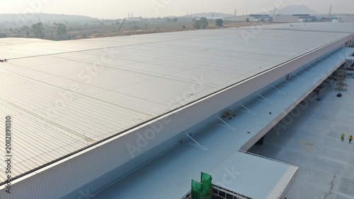 Foto Vast Industrial Warehouse: An expansive, modern warehouse with a long, gleaming metallic roof dominates the landscape, signifying large-scale logistics and industry