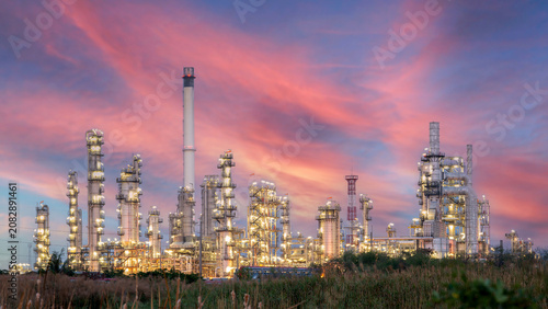 Industrial Powerhouse at Dusk: A sprawling oil refinery complex illuminated against a dramatic sky painted with hues of pink and orange, symbolizing energy production and industrial might.