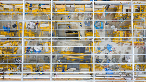 Obraz na plátně Construction Site Aerial View: An intricate aerial perspective of a multi-story construction site, revealing numerous workers and yellow scaffolding meticulously organized across different levels