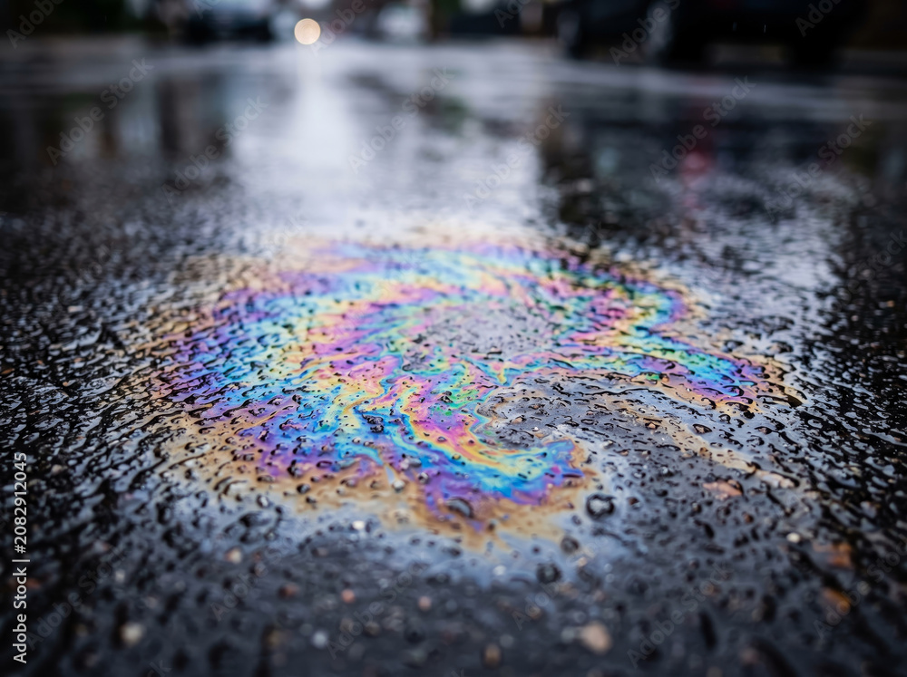 Obraz premium Iridescent colorful rainbow oil spill sheen slick on wet asphalt road surface rainwater