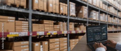 Tableau sur toile Logistics manager dashboard on a laptop beside warehouse shelves and boxes, analyzing inventory, supply chain, and distribution data for monitoring storage and business operations