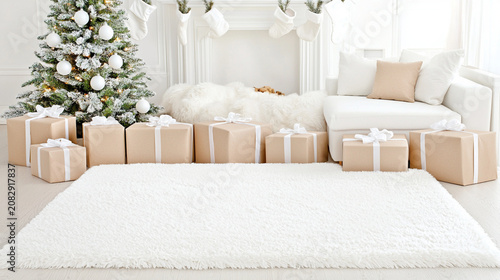 A cozy white living room decorated for Christmas with a frosted tree, stockings, and numerous wrapped presents.