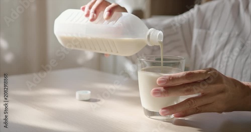 Close up of Asian Woman Hands Pouring Soy Milk into Glass on Table in Cozy Living Room with Warm Morning Sunlight, Healthy Breakfast Routine