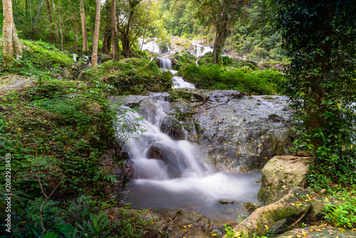 Schilderij op canvas A refreshing stream of Khlong Nam Lai waterfall flowing smoothly over rocks and roots in the lush tropical forest of Khlong Lan National Park, Kamphaeng Phet, Thailand