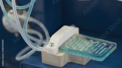 Close up of microfluidic chip and tubing in laboratory, medical research device for fluid control and testing.
