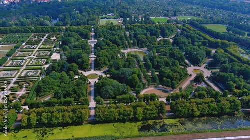 Aerial drone view of Herrenhausen Gardens with tree-lined avenues, fountain pools, and formal baroque parterres in Hannover, Germany, summer daytime.