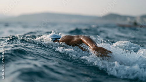 Nigerian open water swimmer mid-stroke in choppy offshore conditions during organized challenge event, support kayak visible nearby, overcast sky, endurance swimming imagery for