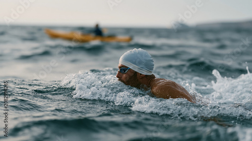 Nigerian open water swimmer mid-stroke in choppy offshore conditions during organized challenge event, support kayak visible nearby, overcast sky, endurance swimming imagery for