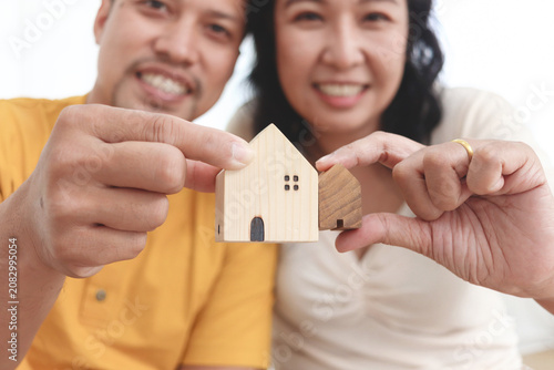 Two decorative wooden houses in hands of middle-aged Asian couple. Happy smiling lovers holding small wooden decorative house in hands. Happy lifestyle, new house concept for a lover investment.