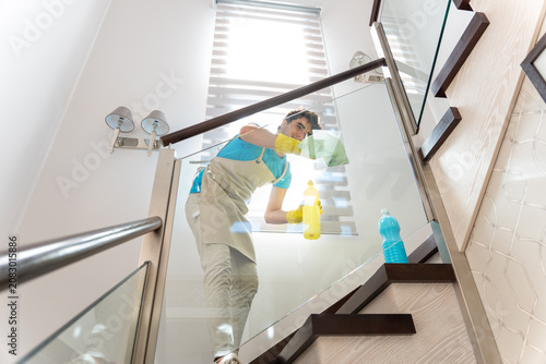 Fotografie Professional cleaner tidying glass staircase railing in modern home